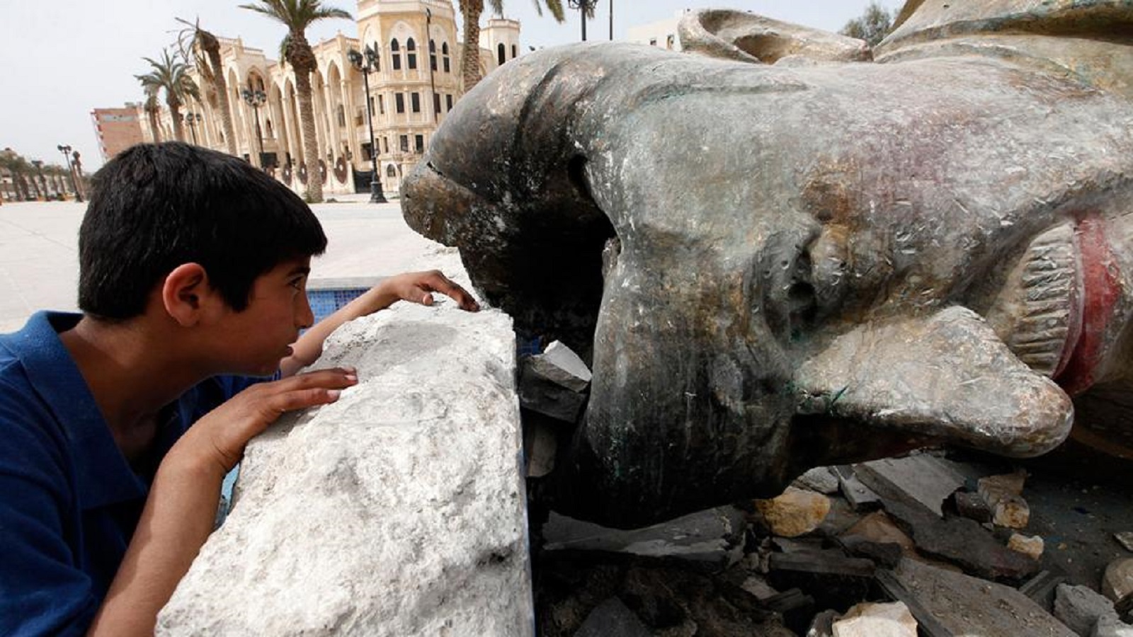 طفل ينظر في جوف تمثال حافظ الاسد المحطم في مدينة الرقة